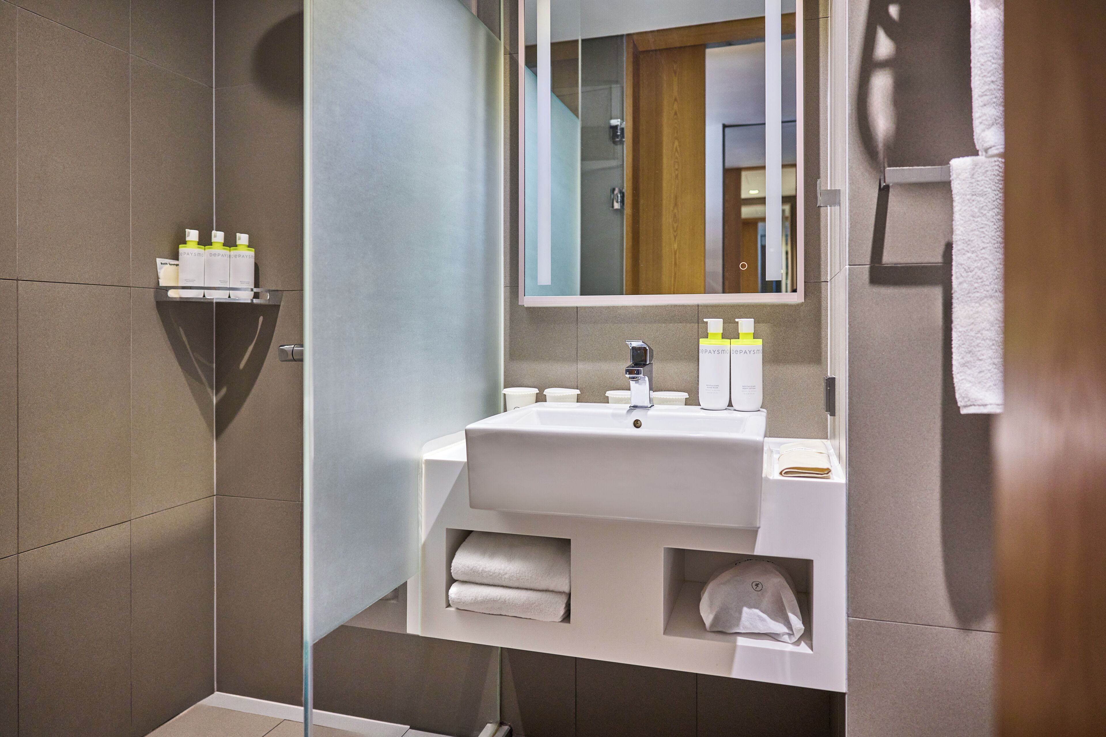 Un baño moderno con lavamanos, espejo, perchero y repisa con artículos de aseo.