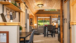 Ein gemütliches Zimmer mit Holzbalkendecke, einem Essbereich mit Stühlen und einem Tisch sowie Blick auf Grünflächen.