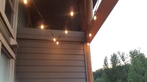 A covered porch with a grill, a bicycle, and string lights. - Fantastic Fernie Flat !! Central Location & Amenities  (Fernie)