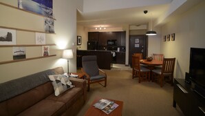 A living room with a sofa, armchair, and coffee table, a dining area with a table and chairs, and a kitchen in the background. - Fantastic Fernie Flat !! Central Location & Amenities  (Fernie)