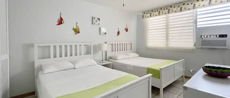 Un dormitorio con dos camas, ventilador de techo, ventana con persianas y radiador.