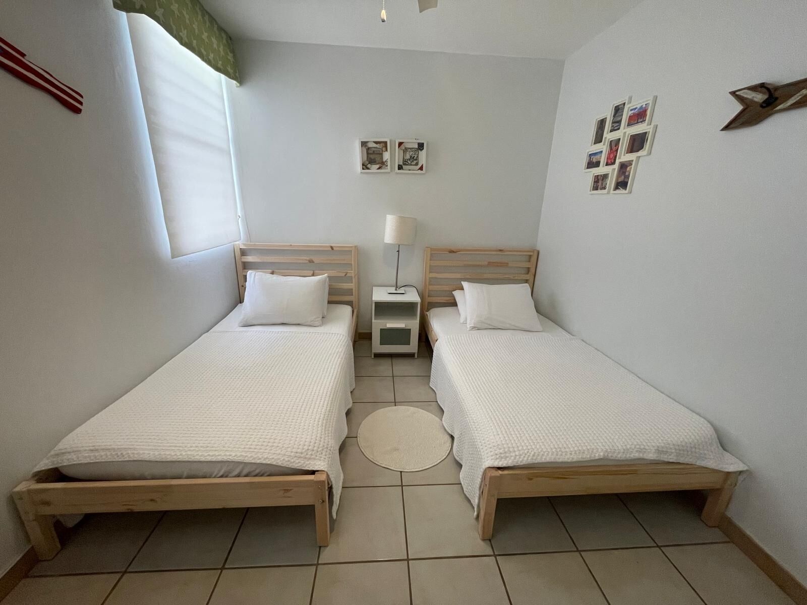 A small, clean room with two wooden beds, a bedside table with a lamp, and a round rug on the floor.