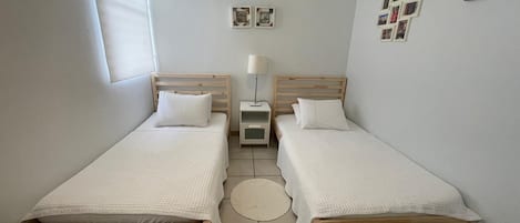 A small, clean room with two wooden beds, a bedside table with a lamp, and a round rug on the floor.