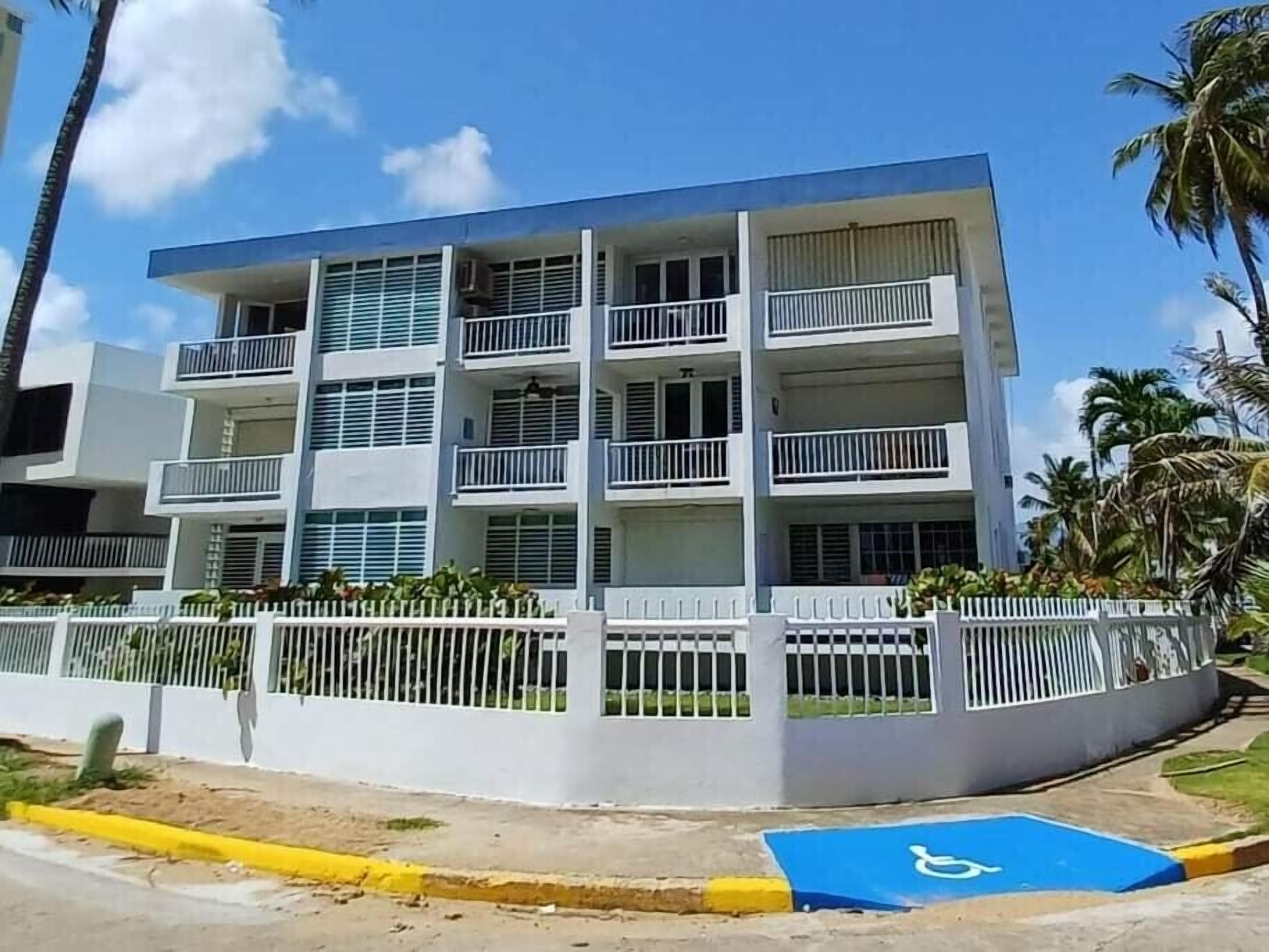 Un edificio de varios pisos con balcones, una cerca blanca y un espacio de estacionamiento para discapacitados de color azul.