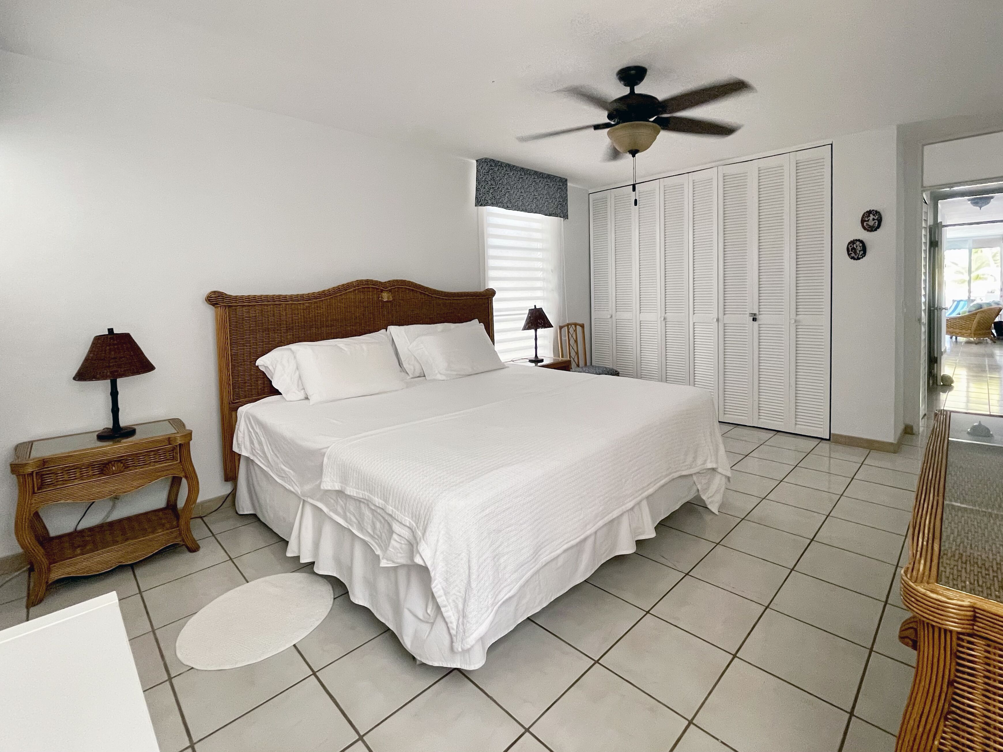 A neatly arranged bedroom with a large bed, a ceiling fan, and a window with blinds.