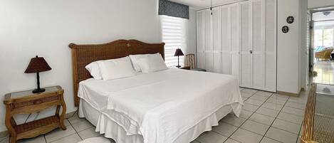 A neatly arranged bedroom with a large bed, a ceiling fan, and a window with blinds.