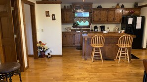 Una cocina con armarios de madera, una isla central con dos taburetes de bar, un refrigerador y un lavabo.