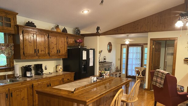 Una cocina con armarios de madera, un refrigerador negro y una isla de madera con taburetes de bar.