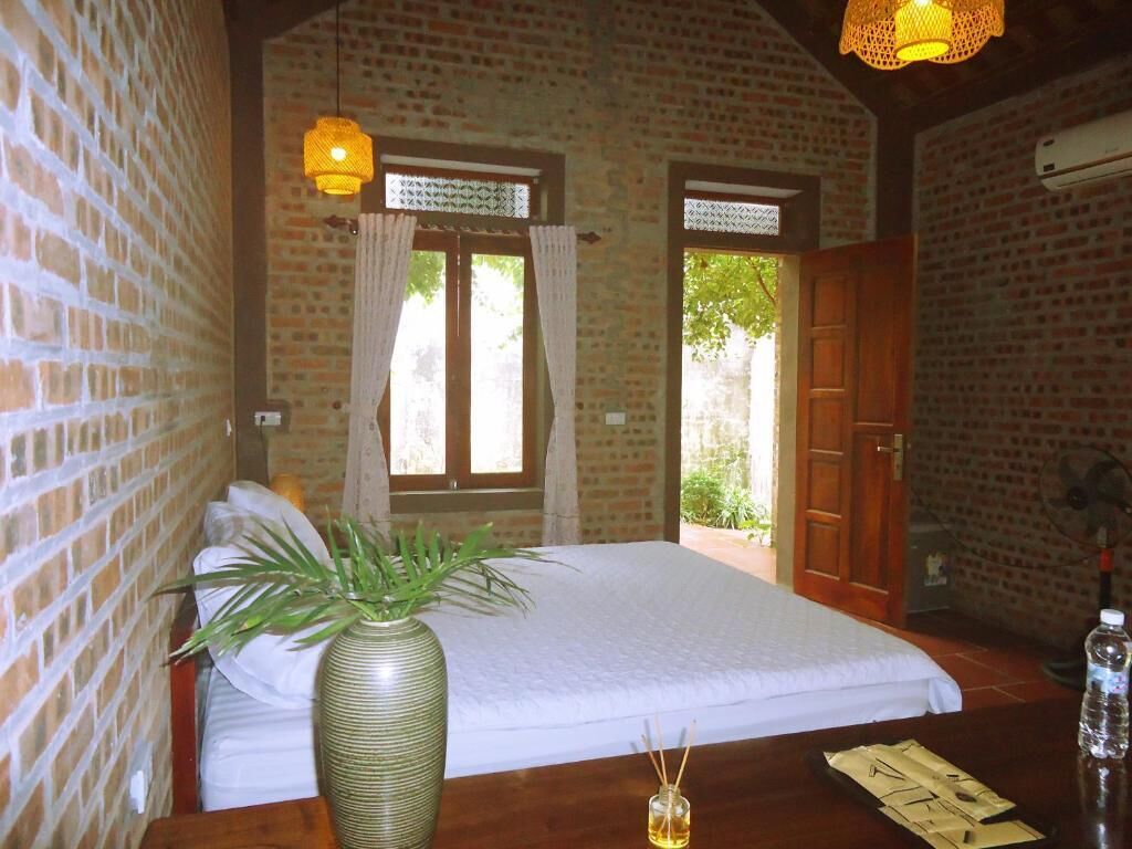 A room with a bed, a wooden table, a potted plant, and a window with curtains.