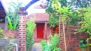 Een klassiek bakstenen huis met een rode deur, een bakstenen trap die naar de ingang leidt en een kleine tuin met verschillende planten.