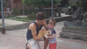 Un homme à genoux sur une surface pavée, avec un enfant et un chat.