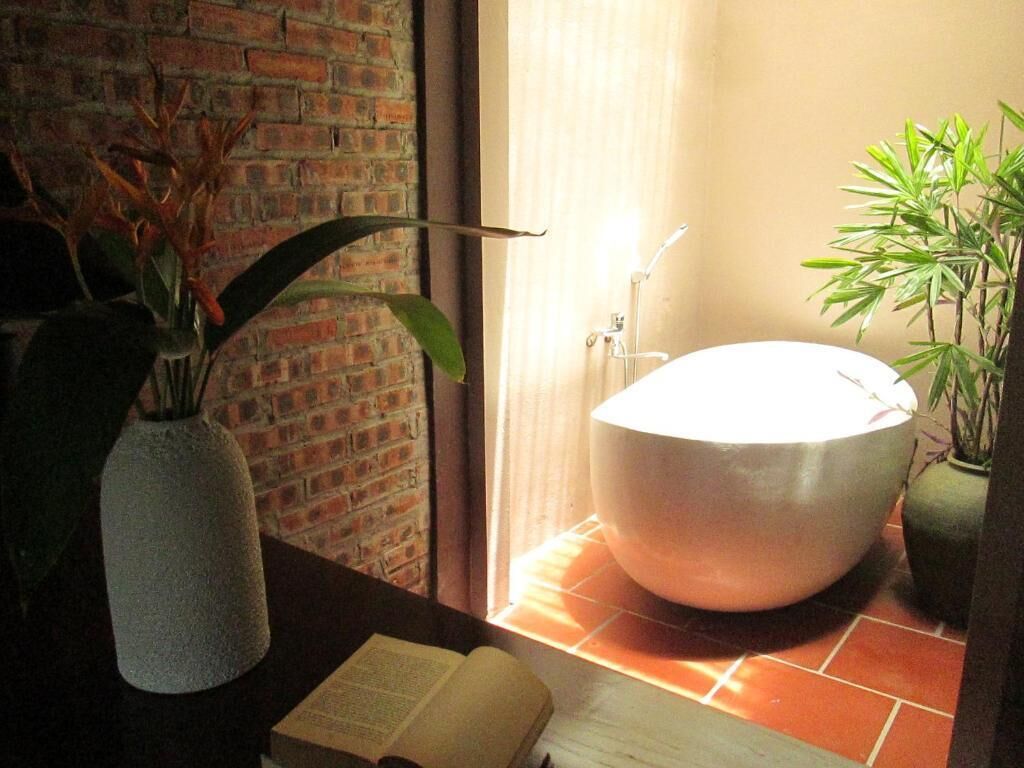 Un baño con una bañera blanca, una planta en maceta y una pared de ladrillo.