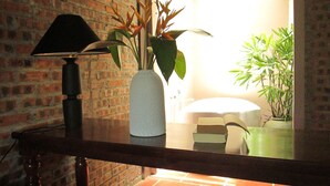 Een badkamer met een bakstenen muur, een wit bad en een groene plant in een grijze vaas.