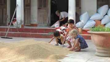 Children playing with grains on a porch with a large planter and bags of grains in the background.