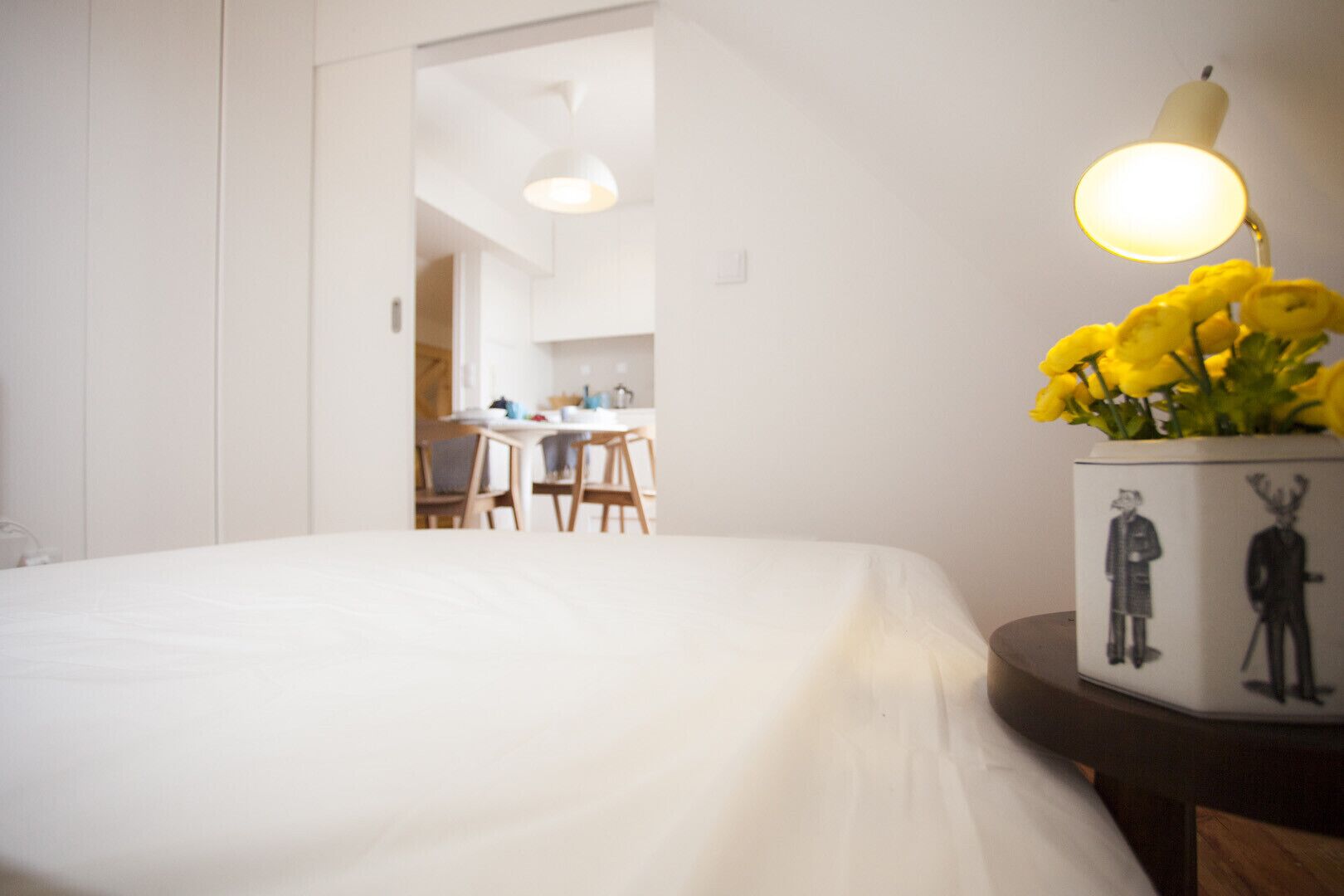 Ein Hotelzimmer mit einem Bett, einem Tisch mit einer Lampe und einer Vase mit gelben Blumen.