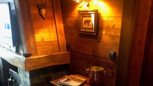 A rustic interior with wooden walls, a bear skull decoration, a framed picture, a table with a book, and two stools. - Triplex apartment in chalet, spectacular view of Megève and the Alps (Demi-Quartier)