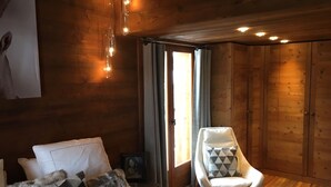 A cozy room with wooden walls, a bed with a patterned blanket, a chair with a geometric cushion, and a painting on the wall. - Triplex apartment in chalet, spectacular view of Megève and the Alps (Demi-Quartier)