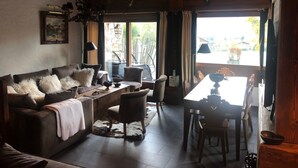 A cozy living room with a sofa, chairs, a dining table, and a view of the outside. - Triplex apartment in chalet, spectacular view of Megève and the Alps (Demi-Quartier)