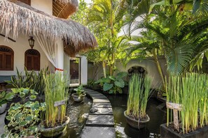 A tropical garden with a thatched roof, a narrow water channel, and potted plants. - Elina Villas (Kerobokan)
