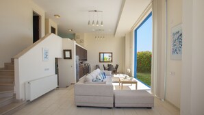 A modern living room with a sofa, a coffee table, and a dining area. There is a staircase leading to another level. - Protaras Fig Tree Bay Seafront Villa Infinite Aretousa (Protaras)