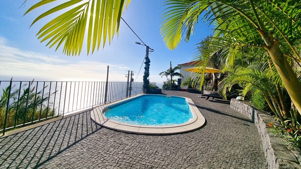 Ein Schwimmbecken mit gefliestem Sonnendeck, umgeben von Palmen und Blick auf das Meer.