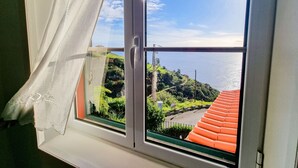 Ein Fenster mit Blick auf eine Küstenlandschaft, darunter ein Gebäude mit rotem Dach und viel Grün.