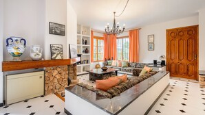 A modern living room with a sofa, a dining table, and a fireplace. There are decorative items on shelves and a large wooden door.
