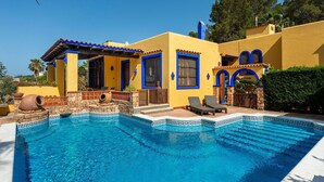 A Mediterranean-style villa with a swimming pool, stone walls, and blue accents.