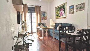 A living room with a blue sofa, a dining table with chairs, a TV mounted on the wall, and a large window with curtains. - Punta Umbria, Huelva Andalucia Costa de la Luz 2 bedrooms swimming pool  (Punta Umbría)