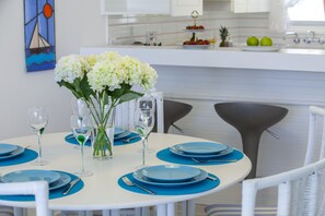 A dining area with round tables set for four, each with blue placemats, white plates, and clear glassware.