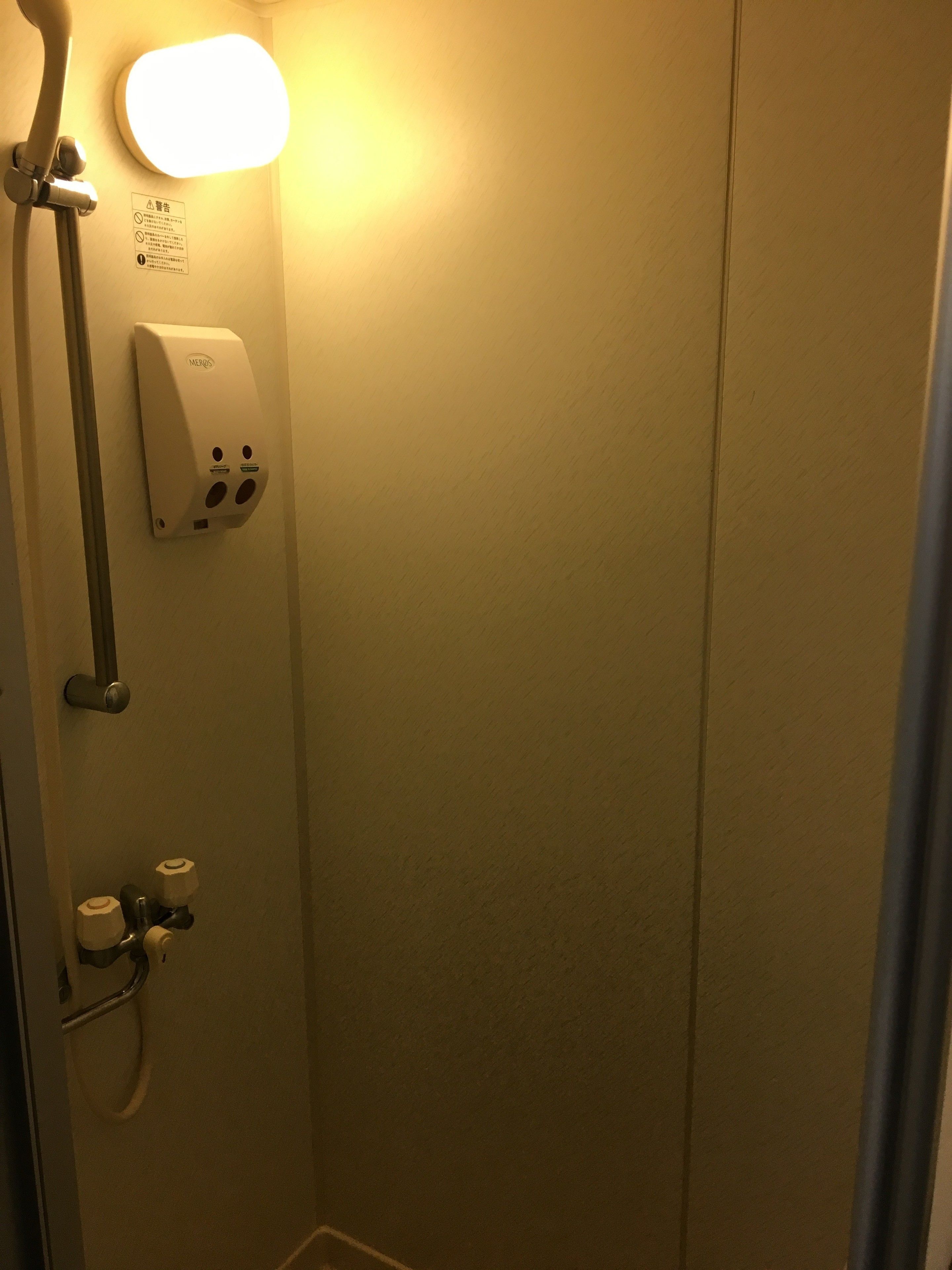 Een douche met een zeepdispenser, een handdoekhouder en een bord aan de muur.