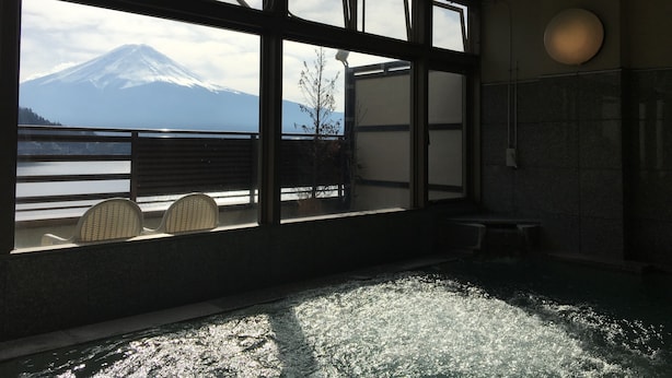 A room with a large window overlooking a mountain and a body of water. There are wicker chairs and a small table by the window. - Tominoko Hotel (Fujikawaguchiko)