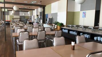 Une cafétéria avec de longues tables et des chaises, un buffet et un comptoir où sont disposés des récipients contenant de la nourriture.