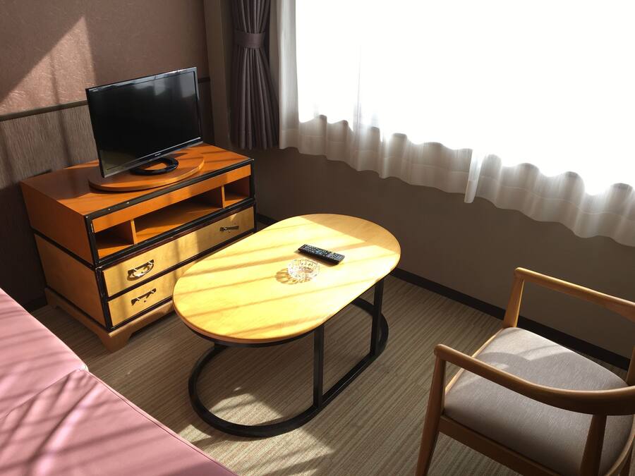 Une chambre d’hôtel avec un bureau en bois, un téléviseur posé sur une commode, une chaise et un lit.