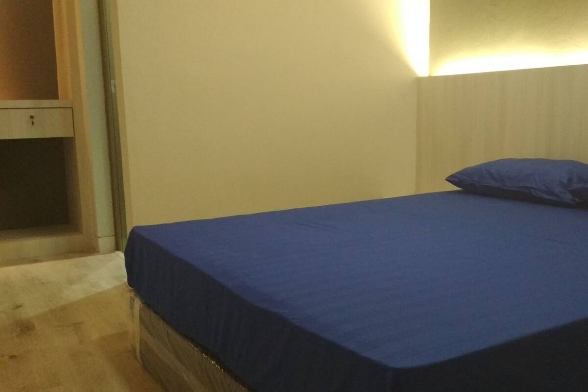 A bedroom with a single bed, a wooden nightstand, and a wall-mounted light.
