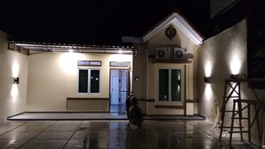 Un edificio con entrada porticada, una motocicleta estacionada afuera y una escalera apoyada en la pared.