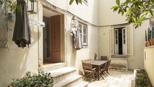 Un patio con una mesa y sillas de madera, una pequeña escalera y plantas en macetas.