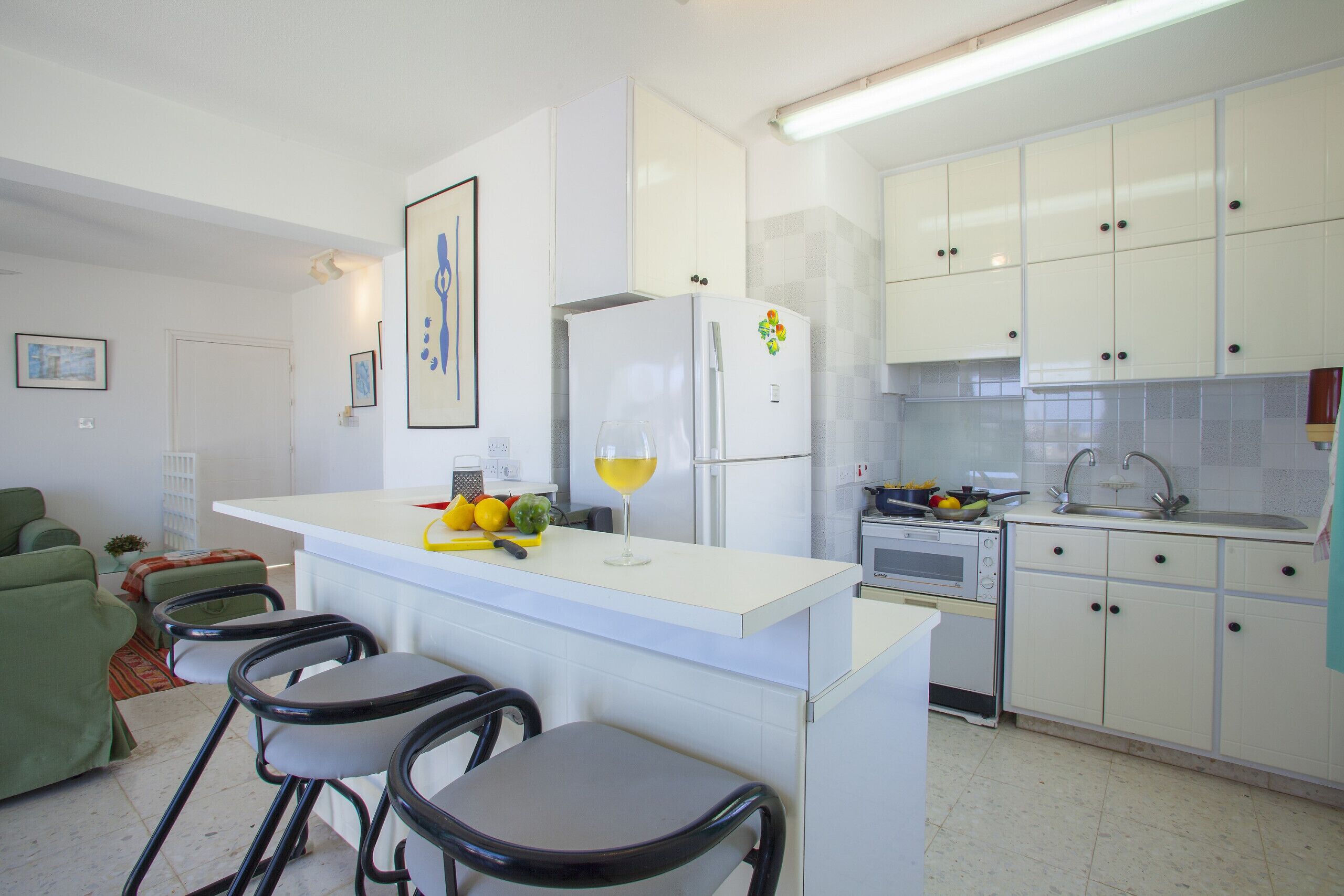 Cocina compacta con isla central, taburetes de bar y muebles blancos.