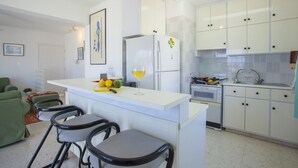 Cocina compacta con isla central, taburetes de bar y muebles blancos.