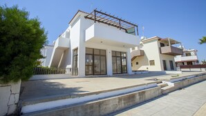 Una casa moderna de dos pisos con balcón, ventanas amplias y entrada pavimentada.