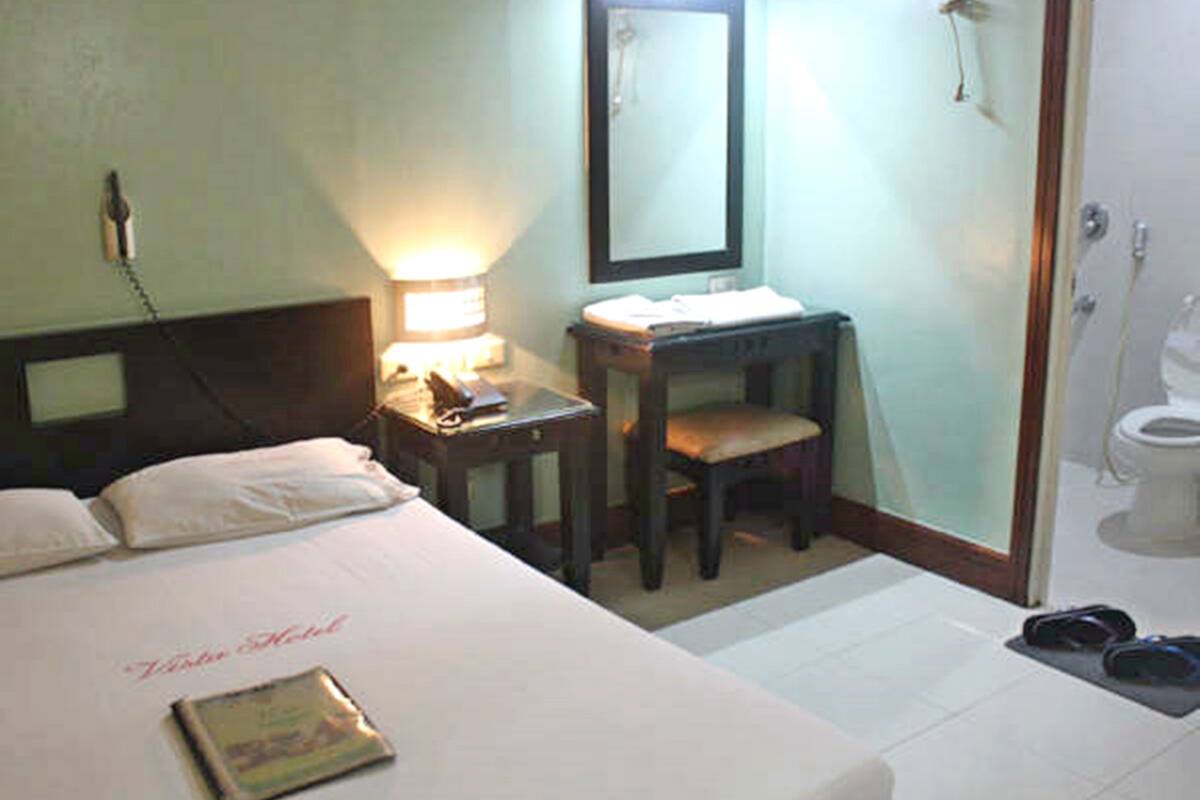 A hotel room with a bed, a desk, a mirror, a telephone, and a shower area.