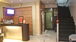 A reception area with a wooden reception desk, a clock on the wall, and a staircase leading to an upper floor. - Vista Apartelle & Restaurant (Makati)