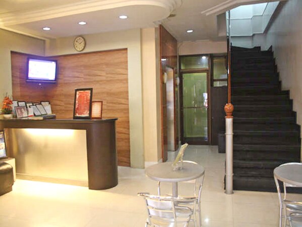 A reception area with a wooden reception desk, a clock on the wall, and a staircase leading to an upper floor.