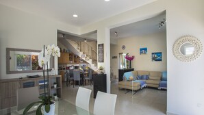Uma sala ampla com uma mesa de jantar, cadeiras, um sofá, escada e uma cozinha ao fundo.