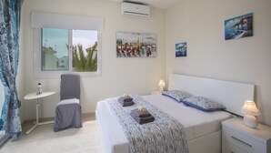 Quarto com cama, mesas de cabeceira, poltrona, janela com vista e obras de arte nas paredes.