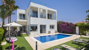Uma casa moderna de dois andares com piscina, área de estar externa e vegetação exuberante.