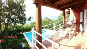 Un'area esterna coperta con piscina, mobili bianchi e vista sul mare.