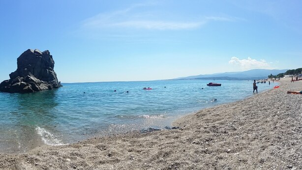 Una costa rocosa con aguas azul turquesa, una destacada formación de roca y una playa de arena.