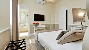 Une chambre d’hôtel comprenant un lit, une télévision, un miroir, une table de chevet avec un vase de fleurs et une chaise.