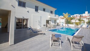 A pool area with lounge chairs and a building with balconies. - Protaras Villa Theodora 1 - CHG (Paralimni)